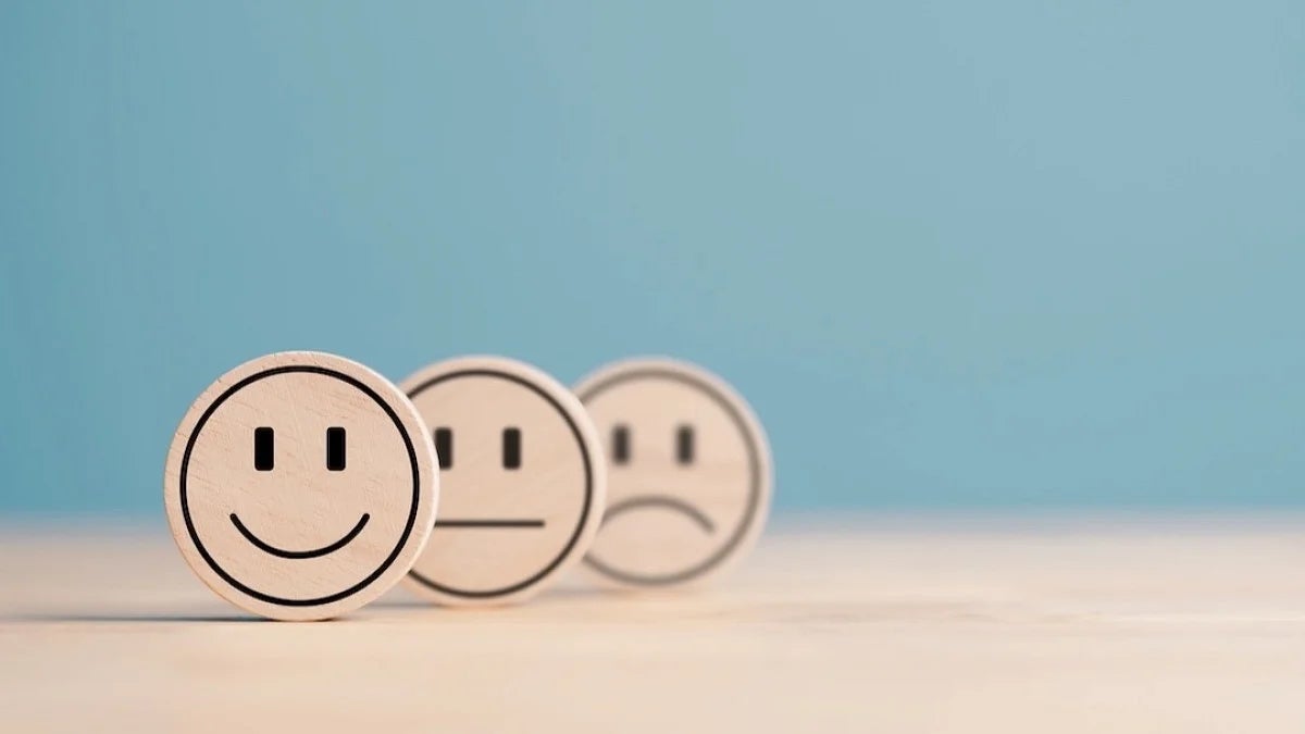 three wooden tokens on a blue background: smile, neutral, frown