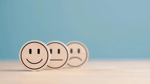 three wooden tokens on a blue background: smile, neutral, frown